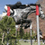 A static image of a large aircraft with red accents on poles, set against trees and mountains under a clear blue sky.