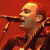 A pixelated contact sheet showing two frames of an animated icon featuring a musician singing into a microphone on the left and green text reading "Original Icons .com" on the right against a dark background.