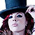 Pixelated close-up of a person wearing a dark blue top hat with red hair visible beneath, against a white background.