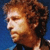Pixelated profile view of a person with curly brown hair against a blue background, wearing a dark top.