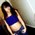 A person in a blue crop top and dark shorts poses against a light-colored wall with subtle shadows.