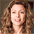 A pixelated close-up of a person with light skin tone, brown curly hair, and a neutral expression, set against a muted brown background.
