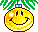 Yellow circular ornament with smiling face hanging from green pine branch, blue cap at top.