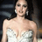 Static 256x256 pixel image of a woman in a white strapless dress with dark hair and earrings against a dark background.
