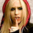 Pixelated static image of a person with long blonde hair featuring red highlights, wearing a dark top with white accents, holding a finger near the mouth in a shushing gesture.
