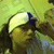 A person with long dark hair wears a white headband with a blue section, positioned against a light green background with blurred figures.