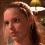 Four- of a person with light brown hair in a braid, wearing a dark top against a blurred background with yellow and white elements