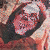 A pixelated image of a person with light skin and dark hair, wearing a white headband, smiling broadly against a blurred background.