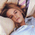 A pixelated close-up of a person with brown hair lying on their back, wearing a light-colored shirt against a blurred background.
