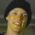 Pixelated close-up of a person with short dark hair, light skin, and a broad smile showing teeth, set against a muted gray background.