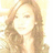 Pixelated image of a person with light brown hair styled in loose waves, wearing a light-colored top against a bright background.