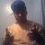 Pixelated image of a person with dark skin wearing a blue cap and light-colored shirt, holding a dark object near their chest.