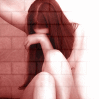 nine identical shows a person with long brown hair covering their face, seated against a brick wall background