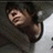 A pixelated image of a person with dark hair and light skin, wearing a dark hooded garment over a white shirt, in two side-by-side frames showing text change.