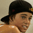 A pixelated image split into two sections: a person wearing a black cap with a yellow emblem on the left, and pink background with text on the right.