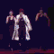 Animated sequence of two figures in white and dark clothing performing synchronized movements against changing colored backgrounds.