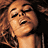 Pixelated image of a woman with curly brown hair, closed eyes, and a smiling expression, wearing a black strap top with visible straps.