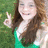 A pixelated image of a person with long brown hair wearing a green top, making a peace sign with their right hand against a blurred green background.