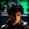 A person with tousled dark hair wears a black jacket with white trim against a green and dark blue background featuring a heart symbol.