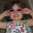 Pixelated image of a person with dark hair wearing pink sunglasses and a colorful patterned shirt, hands raised near head.