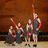 Four distinct scenes displayed in a : performers with red ribbons, people wearing medals, group hugging, and abstract color gradient