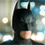 A pixelated figure in a black cowl with pointed ears, wearing a dark suit, positioned against a blurred background with light and blue tones.