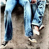 A person wearing blue denim jeans and black-and-white sneakers stands on a textured ground surface.