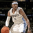 A basketball player in a white uniform with blue accents holds an orange ball, wearing a headband and wristbands.