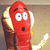 Red cartoon character with wide eyes and open mouth, holding a golden object against a beige background.