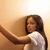 A person with long dark hair in a white shirt extends their arm against a light brown wall, captured across four showing subtle pose and expression shifts