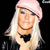 Pixelated static image of a person with long white hair wearing a light pink head covering and black bow tie against dark background.