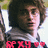 Pixelated image of a person with curly brown hair wearing a dark jacket over a white shirt, with red text and heart symbols at the bottom.