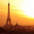 Pixelated image of a tall tower against an orange-yellow gradient sky with dark silhouetted structures below.