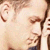 Pixelated close-up of a person's face with light skin tone, brown hair, and visible ear, wearing a dark blue garment with a white collar.