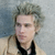 Static 50x50 pixel icon showing a person with light skin, short dark hair styled upward, wearing a black tie and light-colored jacket over a white shirt against a blurred background.