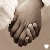Two hands clasped together in a light brown background with subtle white fabric texture, one hand slightly overlapping the other.