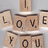 Pixelated wooden blocks spell 'LOVE YOU' with a small 'I,' above black background text reading 'At least Thats what I Thought.'