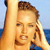 Pixelated close-up of a person with light brown hair holding a phone to their ear against a blue sky and water background.