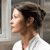 Pixelated profile view of a person with dark hair tied back, wearing a white top, against a blurred background with vertical light and dark elements.
