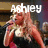A woman with long blonde hair sings into a microphone, wearing a black dress with white and red accents.