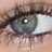 Pixelated close-up of a human eye with dark eyelashes, a grayish-blue iris, and a white sclera, set against a light brown background.