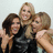 Two identical groups of four people in black outfits pose together with arms around each other against a light background.
