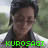Pixelated portrait of a person with dark hair and glasses, wearing a dark jacket over light clothing against an outdoor background.
