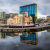 Pixelated static image of a cityscape with a bridge over water, featuring blue and brown buildings under a light blue sky.