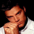 Pixelated static image of a person with light skin tone wearing white clothing, resting their chin on one hand against a black background.