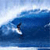 Pixelated static image of a surfer riding a large blue wave with white foam, set against a light sky background.
