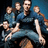 Pixelated image of multiple figures in blue attire with light-colored limbs against a dark background, appearing to be part of a group pose.