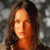 A pixelated close-up of a person with long brown hair against a blurred gray background, showing warm skin tones and closed eyes.