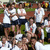 Group of people in white shirts and dark shorts standing on a grassy field with text overlays.