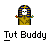 Pixel art icon of a mummy-like figure with skull face, blue-and-gold striped headdress, and outstretched arms holding red/blue gems, below text reading "Tut Buddy" on gray background.